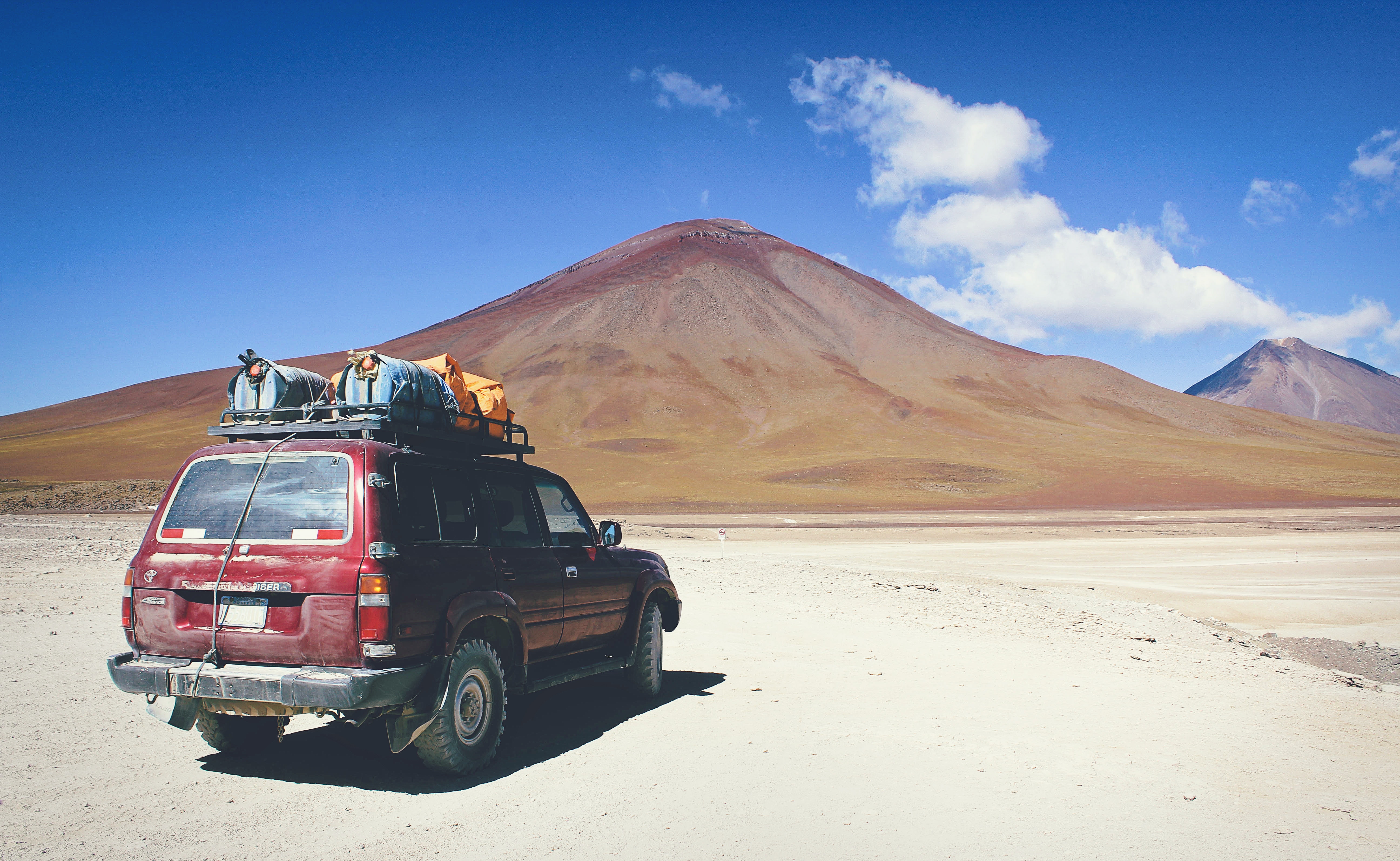 Dirty red Toyota hatchback with supplies on top overlooks mountains in the distance