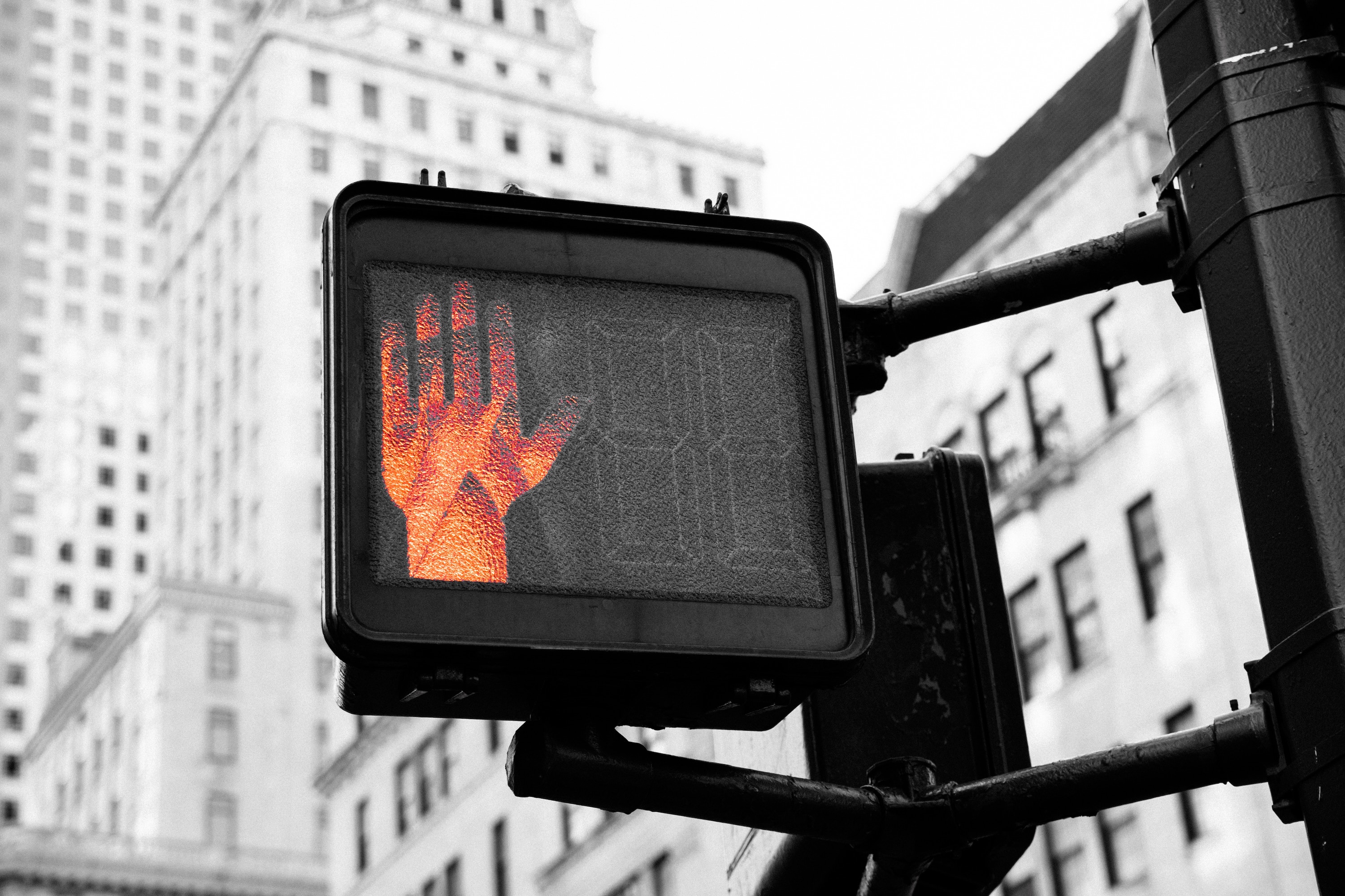 Black and white photo of a street crossing sign with the stop hand signal in red