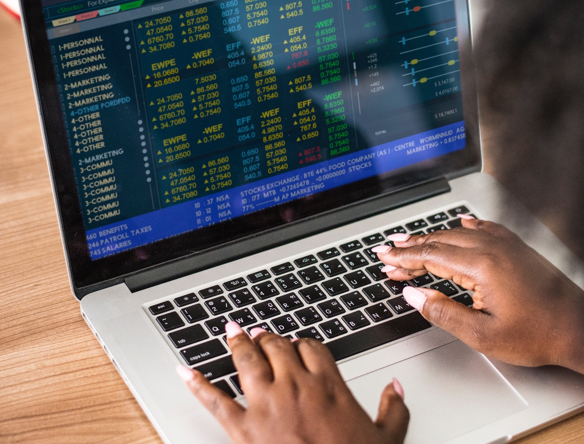 Black woman types on her laptop while her screen shows updated stock market numbers