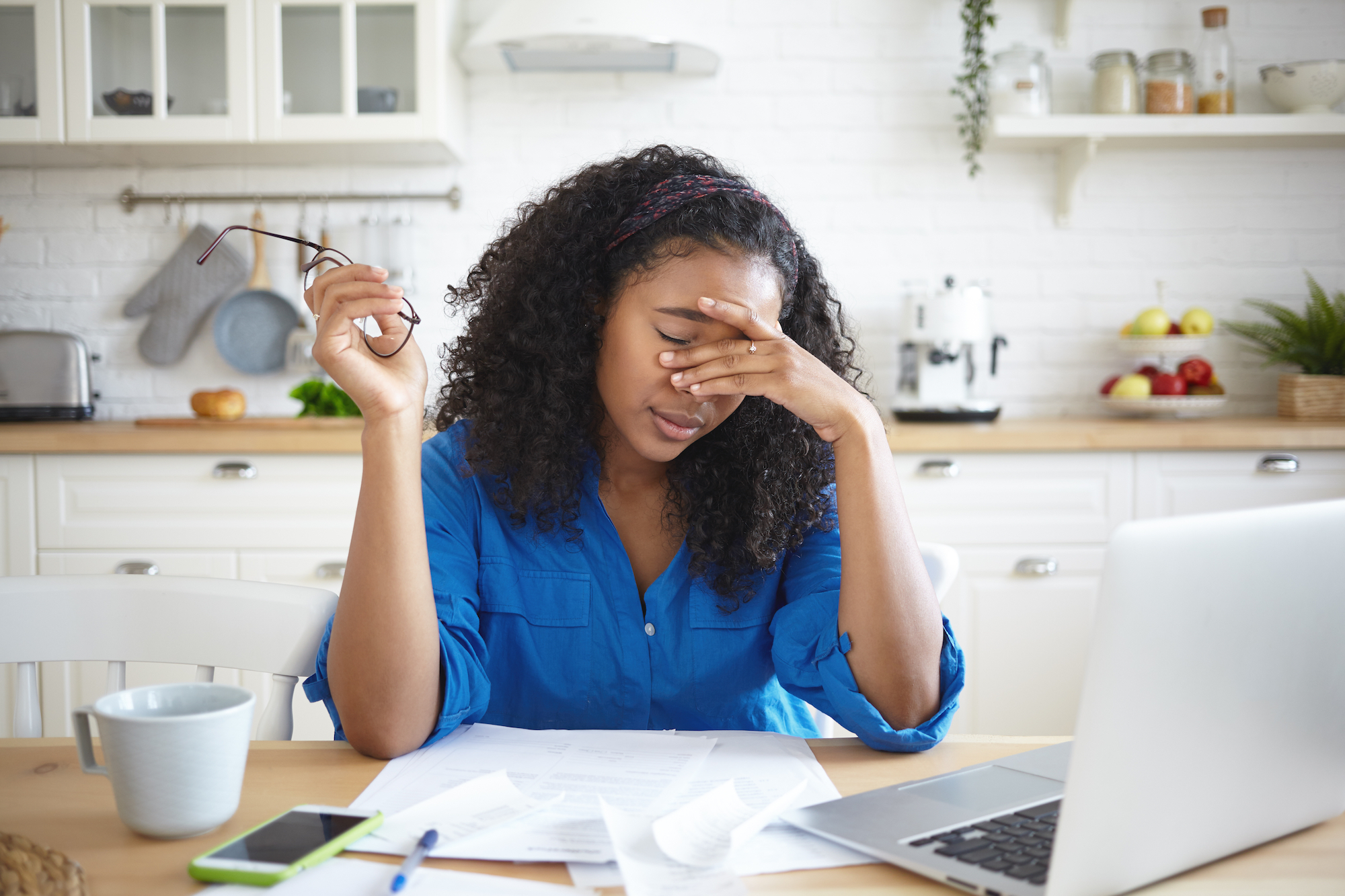 Black woman in a blue button down shirt looks stressed with her left hand o...