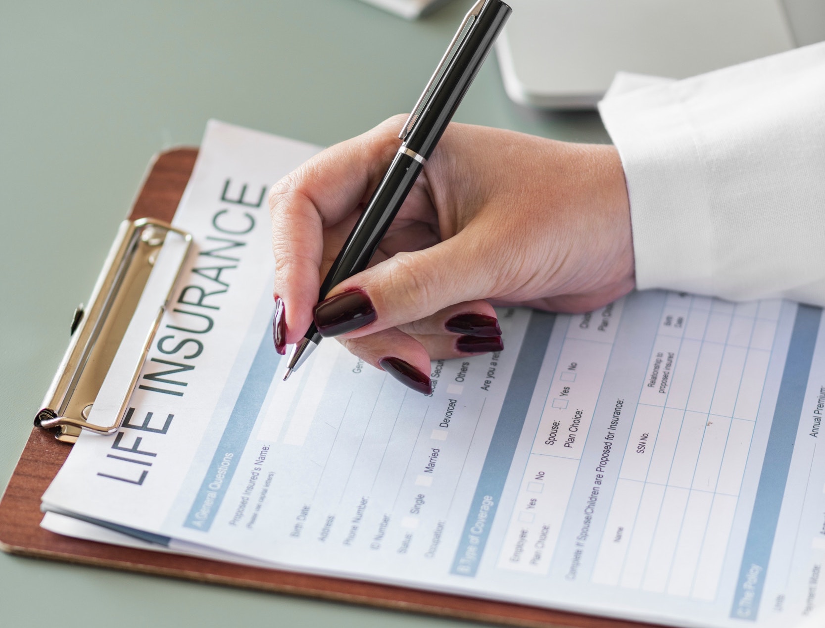 White woman with wine colored nails holds a pen while she fills out a life insurance form