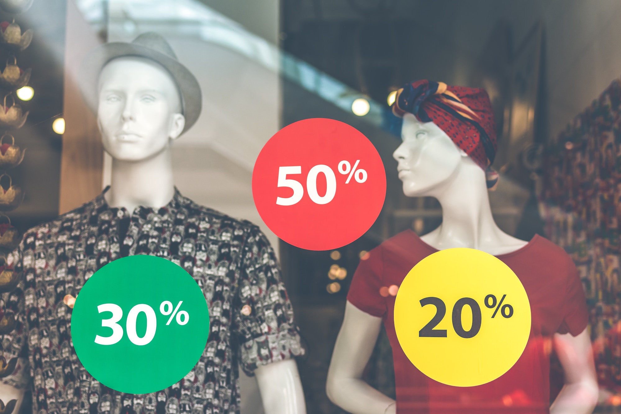 Storefront of two mannequins with stickers showing various percentages indicating a sale