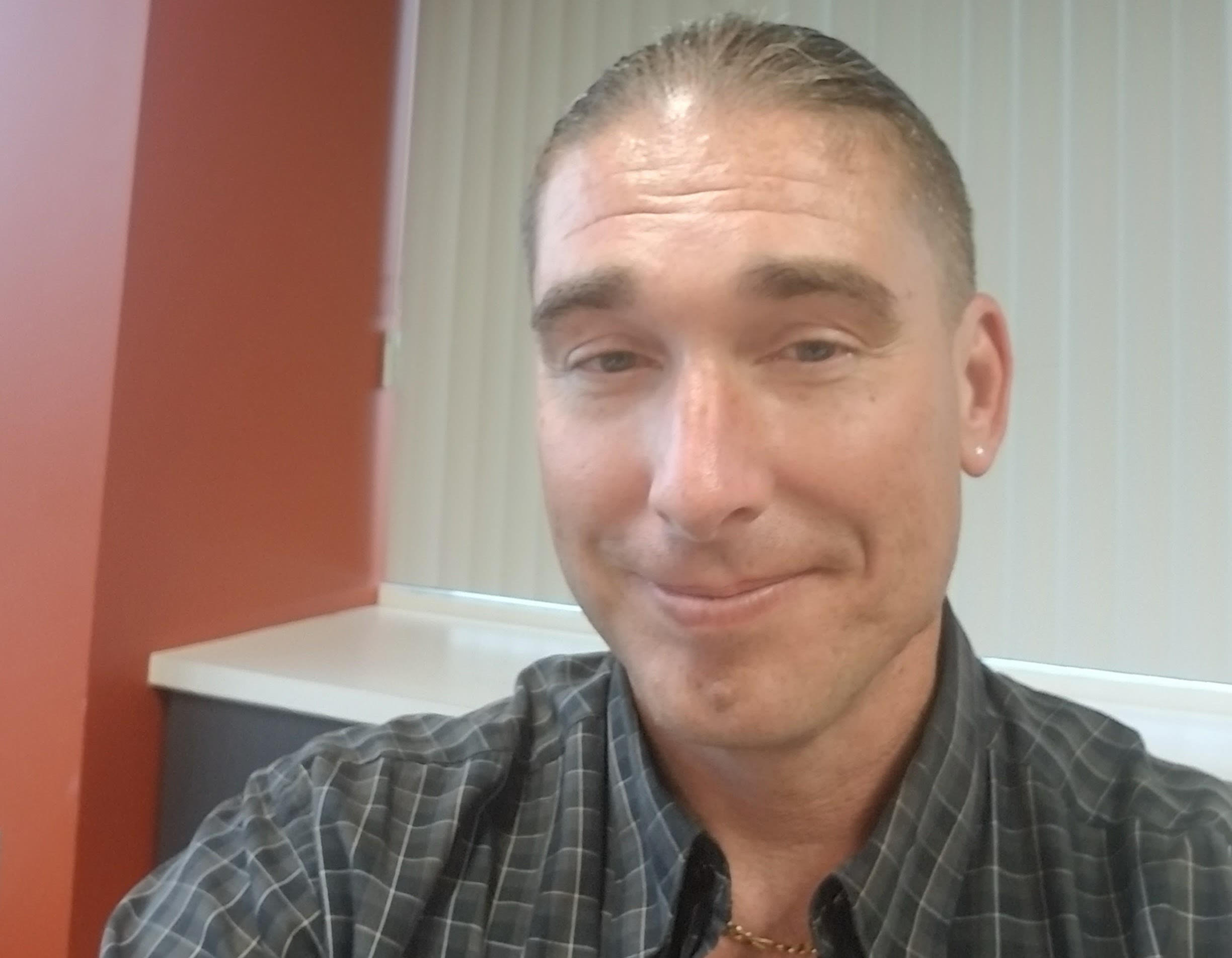 Middle-aged white man with his hair slicked back wears a long sleeve t-shirt and smiles for a selfie