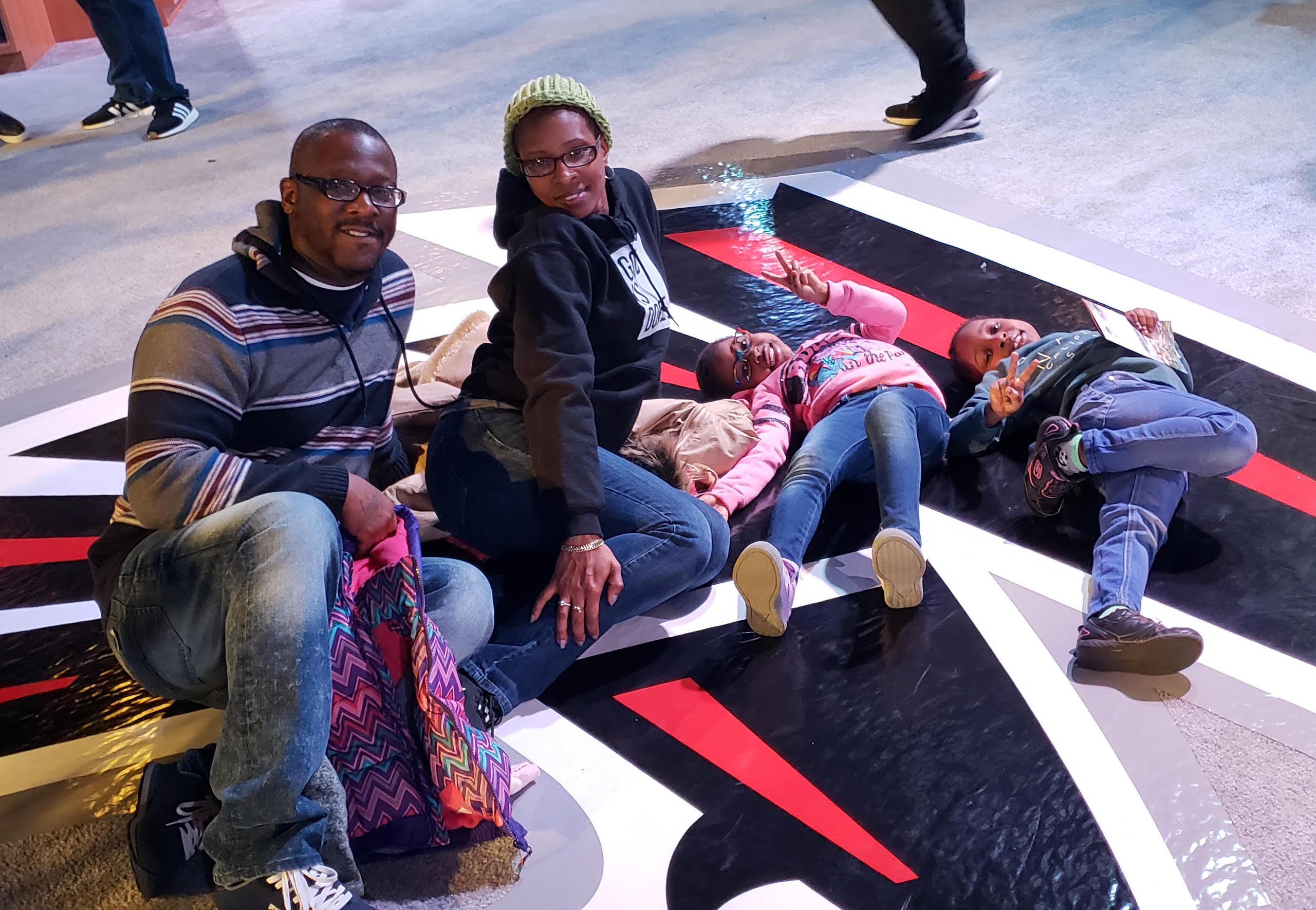 A black family dressed warmly sits on the floor of a basketball court