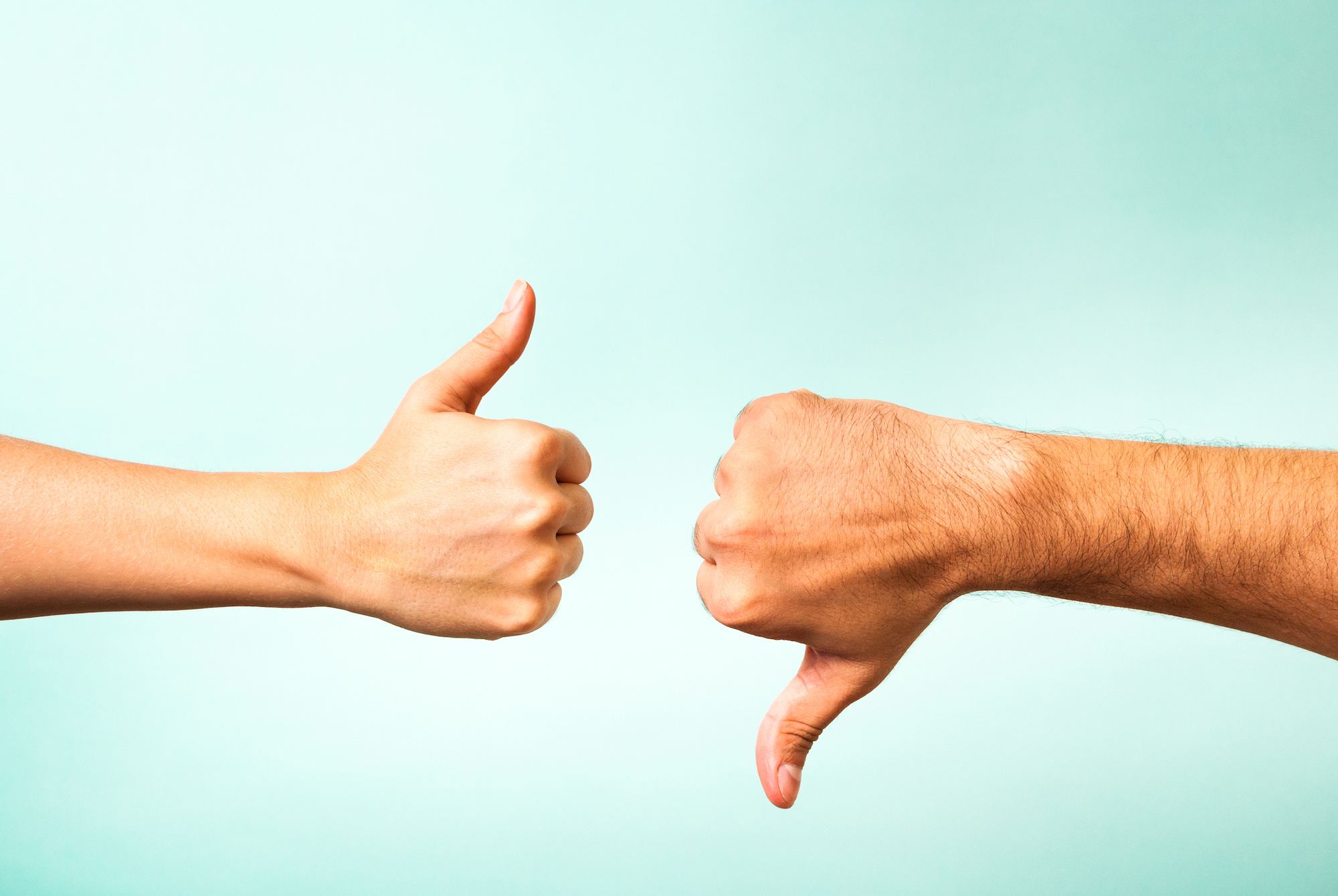 A woman's hand gives a thumbs up opposite of a man's hand giving a thumbs down on a teal background