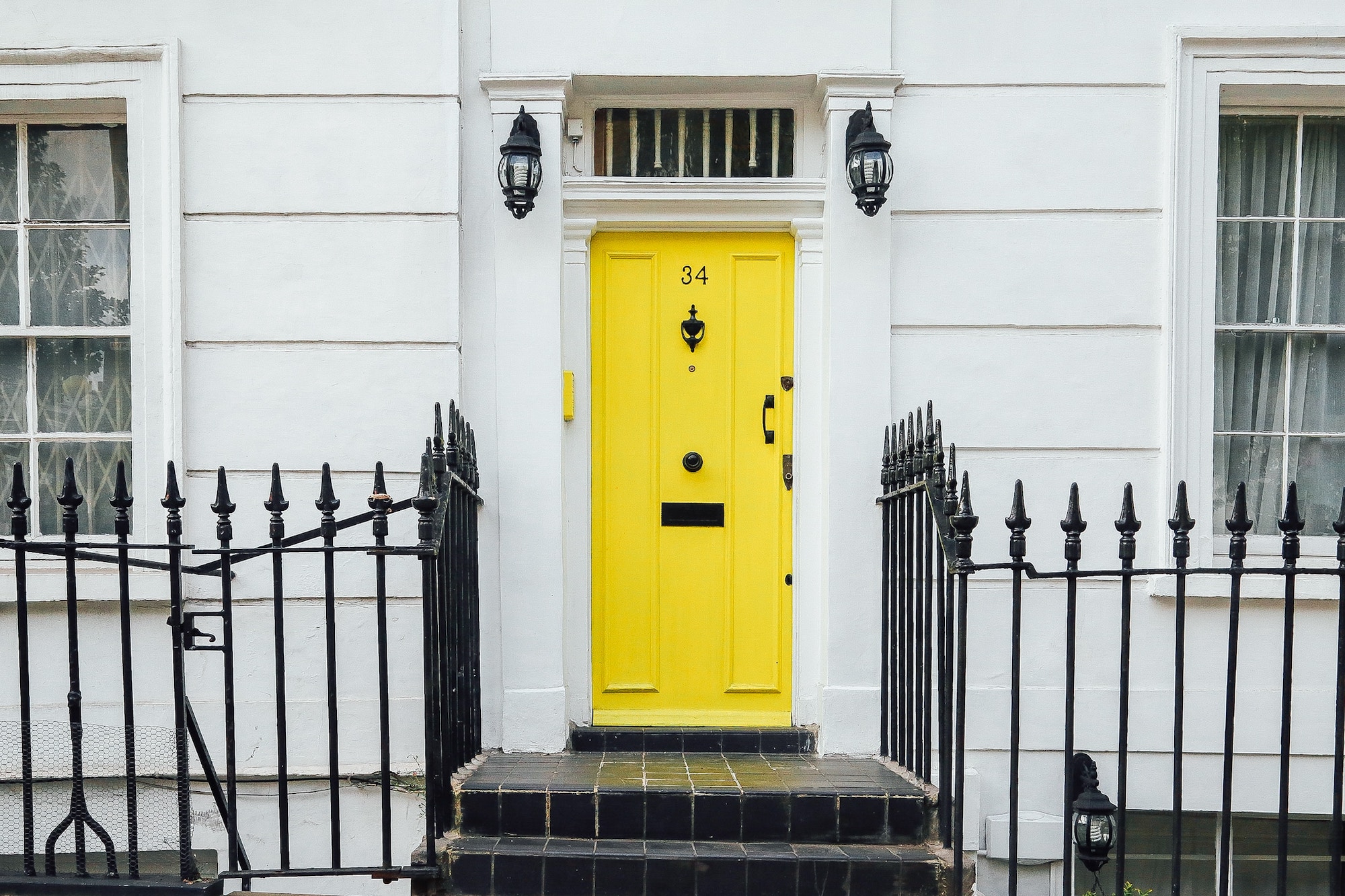 Symmetrical photo of a yellow door of a white house with fences on either side