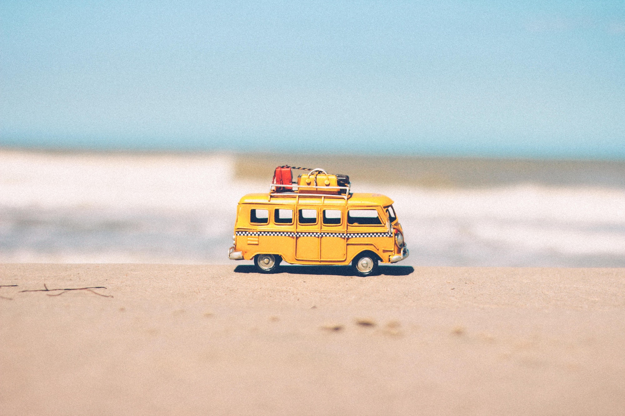 Yellow toy van carrying luggages placed on the sand of a beach with the waves crashing in the background