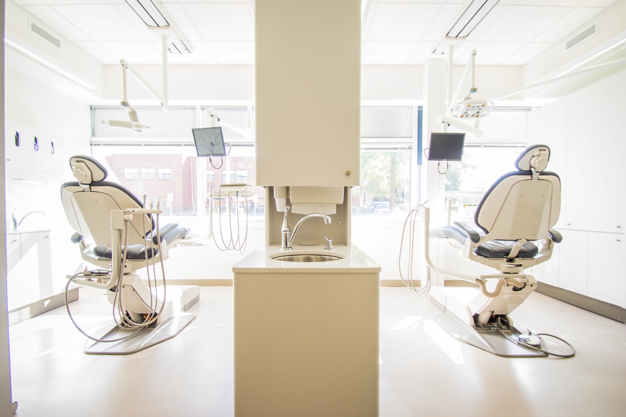 Two vacant patient seats are facing a big glass window at a dentist office