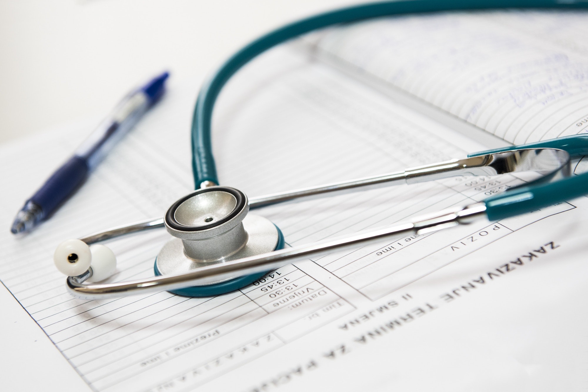 A teal stethoscope and pen are arranged neatly on a doctor's notes for a patient