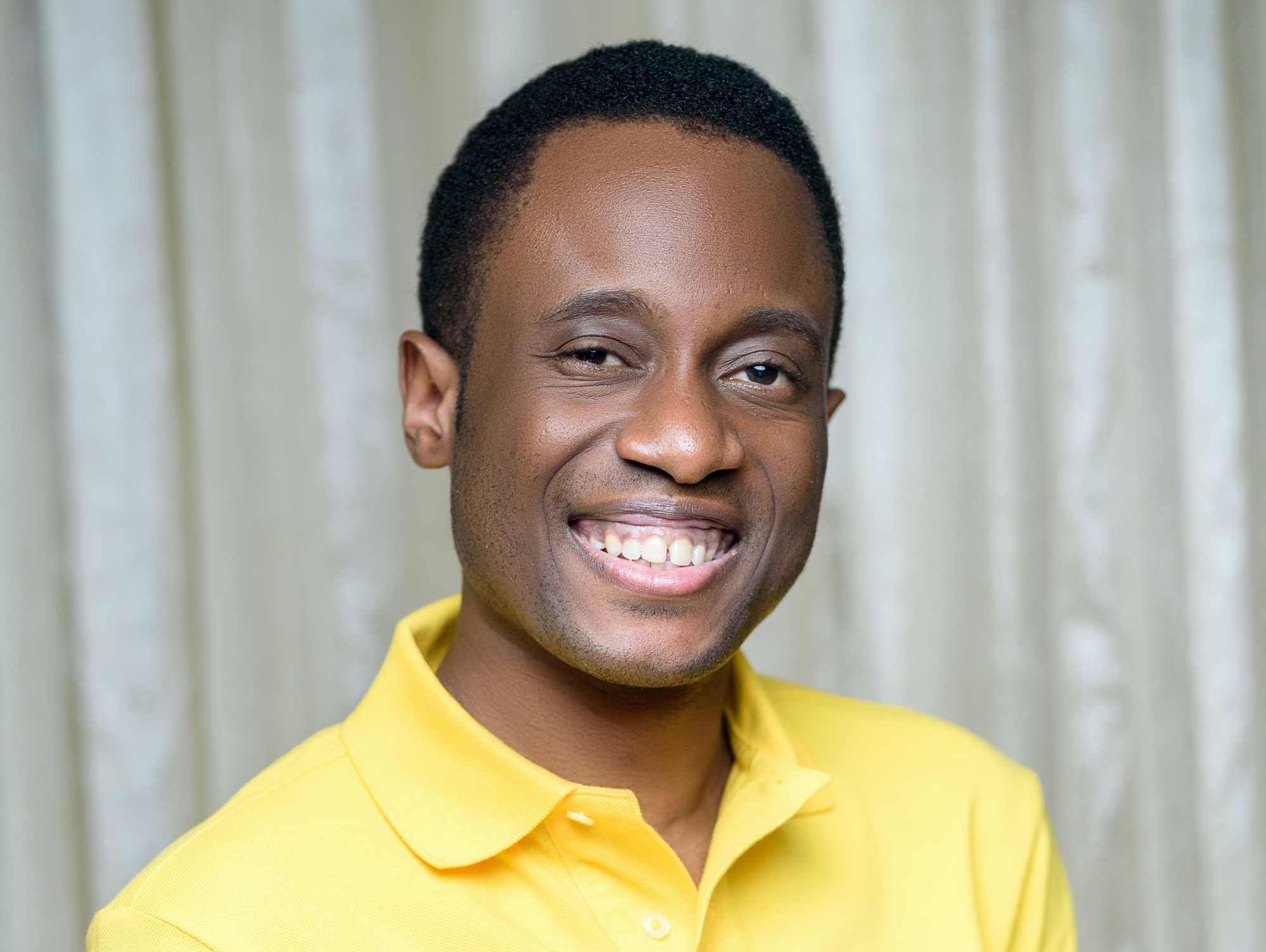 Headshot of an African-American man in a professional studio who wearing a yellow polo and smiling