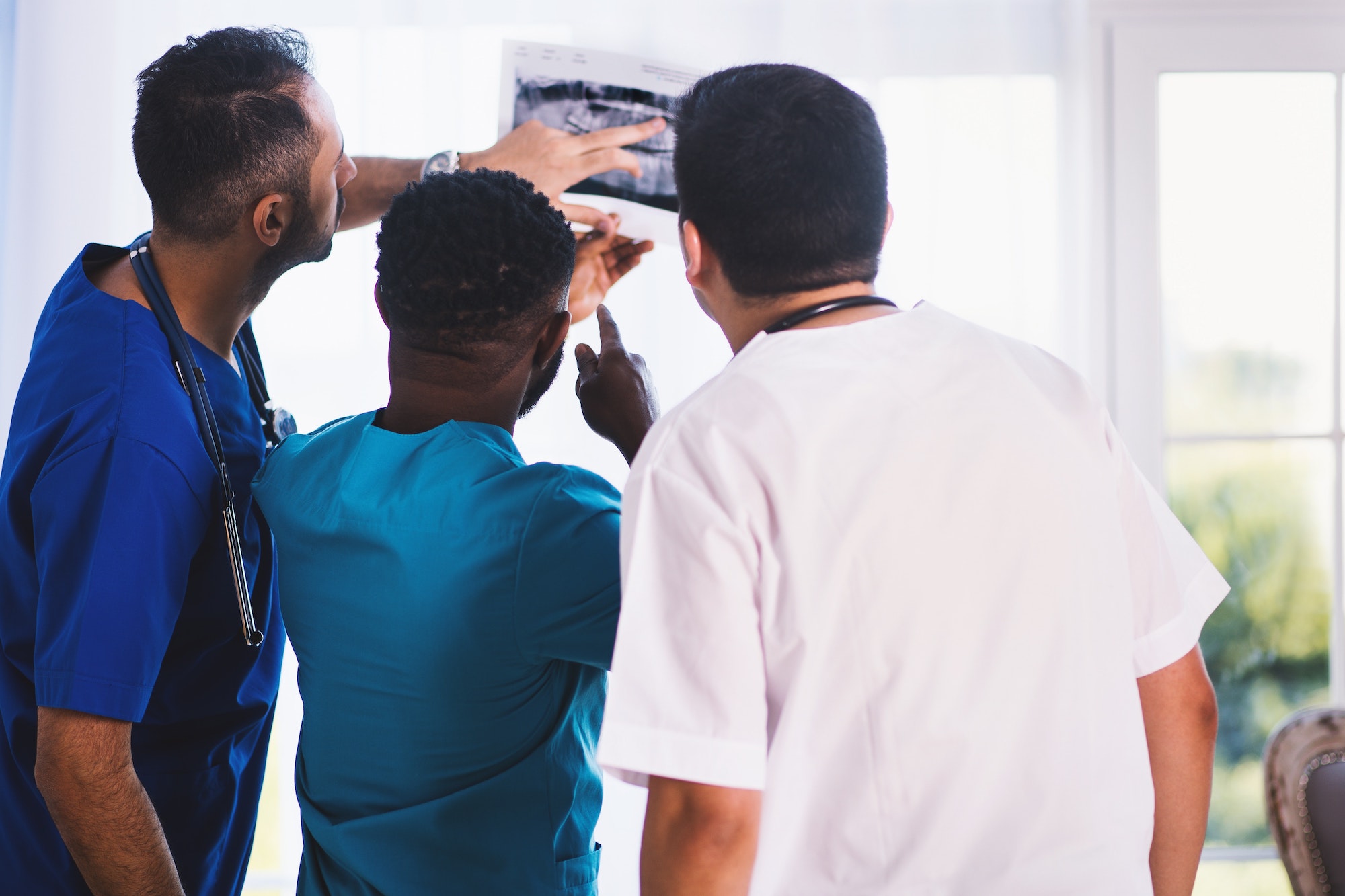 Three doctors of color wearing different colored scrubs looking intently at an x-ray in a hospital