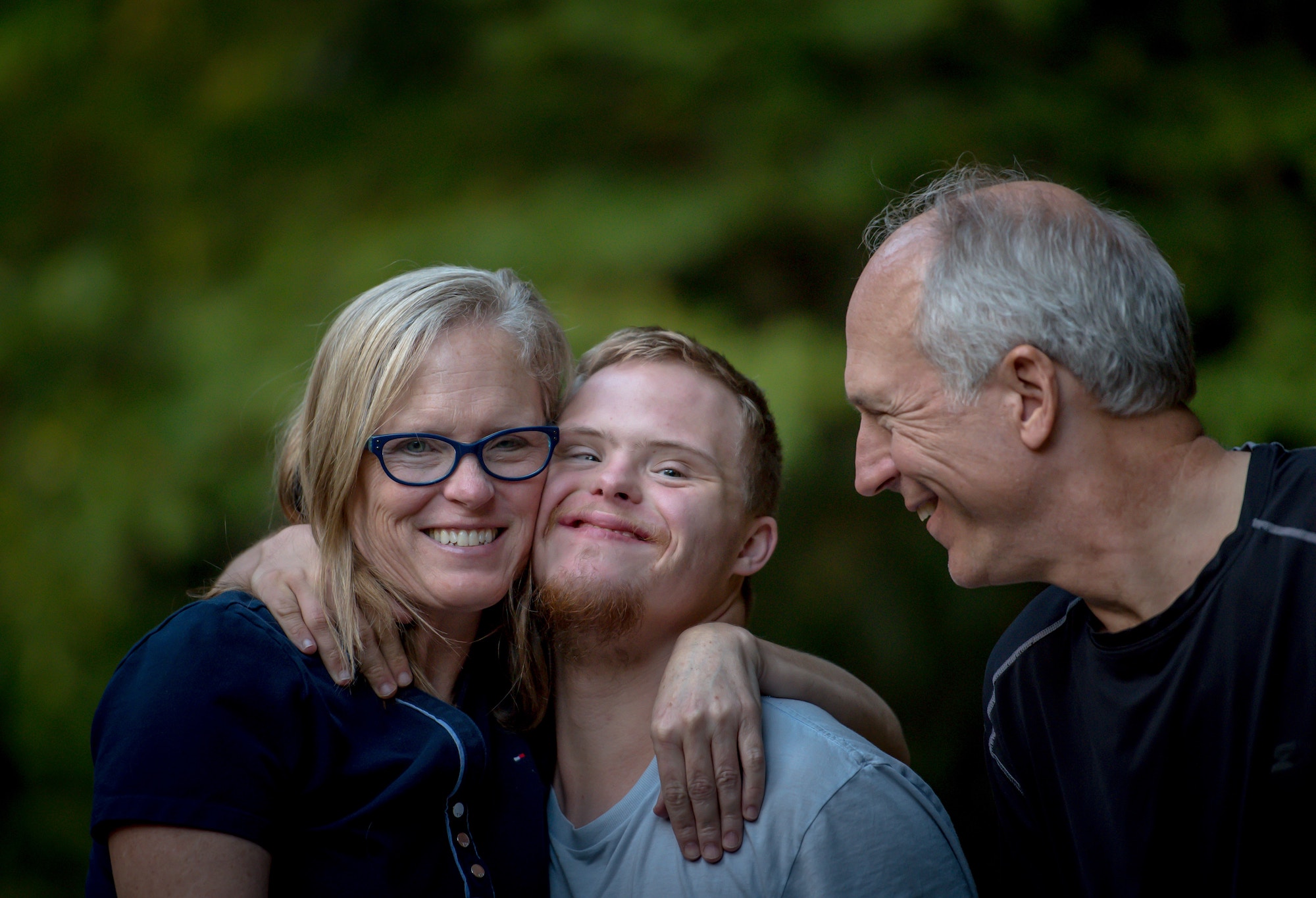 Family made up of a mother, father, and son, who has Down Syndrome, hug one another outside