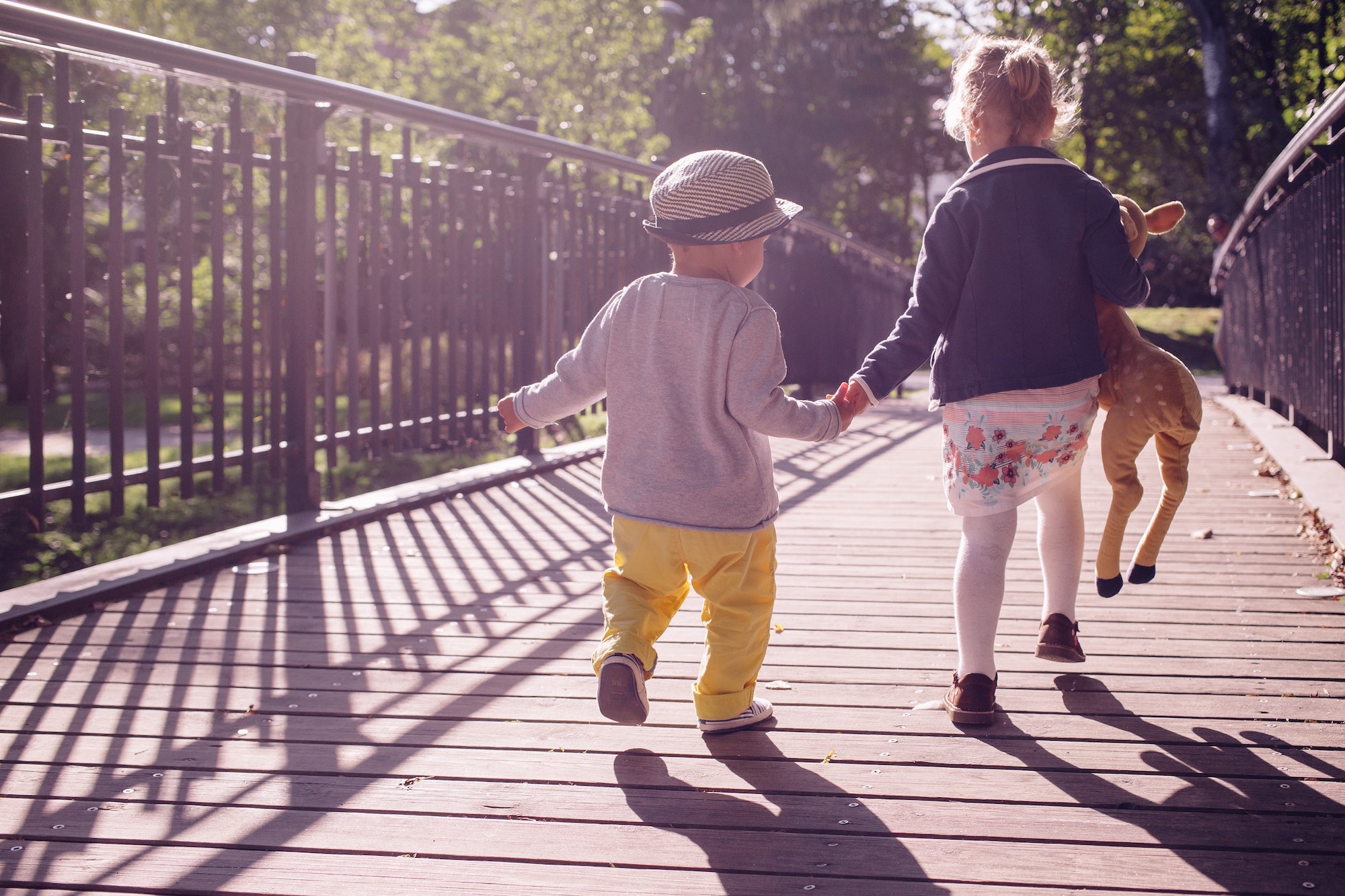 Two young children happily running across a bridge together holding hands